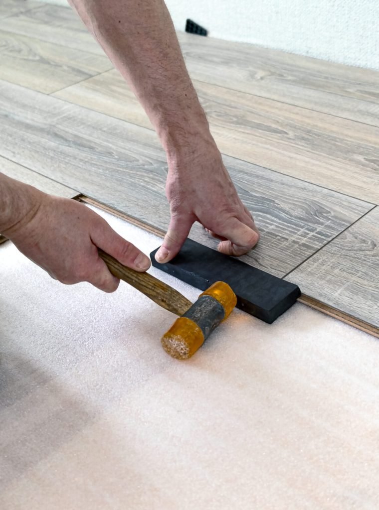 The master does the work of laying the floor laminate, a special tool in his hands